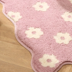 Pink floral non-slip plush bath mat with wavy edges on a light brown wooden floor