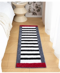 Close-up of plush bedside rug with black white stripes and red accents on wood floor