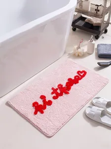 Dettaglio del tappeto da bagno rosa con scritte rosse in rilievo e trama assorbente