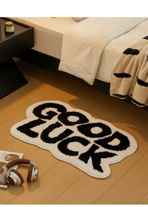Detail of a wavy cloud-shaped plush bath mat with Good Luck bold text on wooden floor