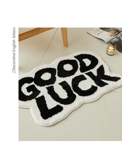 Macro detail of plush GOOD LUCK letter absorbent mat with wavy edges in cozy home setting