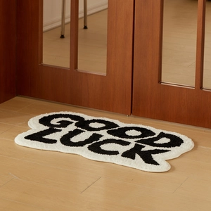 Black and white Good Luck letter shaped absorbent bath mat on wooden floor