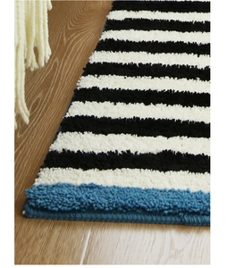 Close-up of thick striped microfibre rug with blue edging on wooden floor