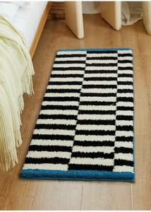 Close-up of thick tufted rectangular bedside rug with black white stripes and blue edges