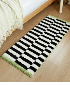 Detail of plush black and white striped bedside rug with green edges on light wood floor
