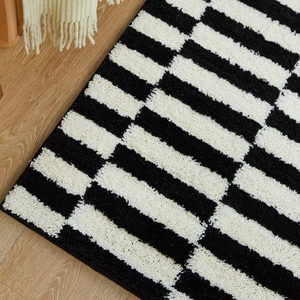 Thick black and white geometric striped runner rug on light wood floor in bedroom