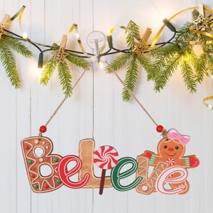 Détail d'une pancarte de Noël 'Believe' en bois style pain d'épices sur mur en bois blanc