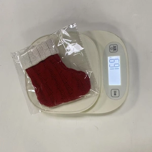 Dettaglio di una mini calza natalizia in maglia su una bilancia che pesa esattamente 16,9g