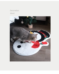 Detailed view of snowman-shaped tufted bath mat on dark wood floor with festive cat