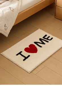 Détail d'un tapis de bain moelleux avec slogan I love ME posé sur un sol de chambre