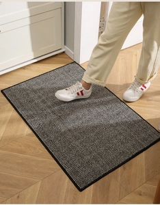 Detailed texture of black and white striped doormat on wooden floor with walking sneakers