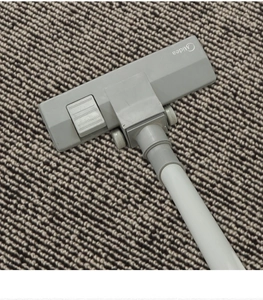 Close-up of a gray vacuum cleaner floor brush nozzle on a striped carpeted surface
