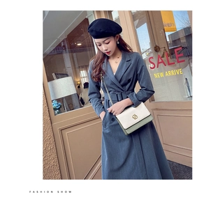 Détail d'un sac bandoulière chic crème et vert sauge avec un trench-coat bleu-gris élégant