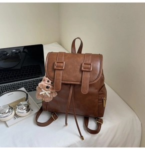 Detail of vintage brown PU leather backpack with belt straps and plush bear charm