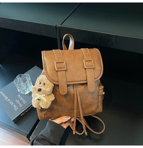 Detail of vintage brown leather backpack with drawstring closure and cute plush bear pendant