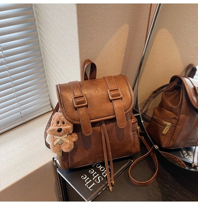 Detail of dark brown leather backpack with drawstring closure and plush bear charm