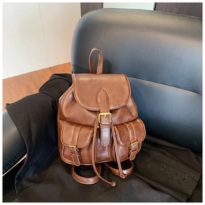 Detalle de mochila vintage marrón con correas de hebilla y bolsillos frontales en una silla