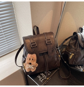 Detail of coffee brown PU leather backpack with vintage buckles and a plush dog pendant