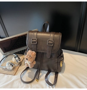 Detail of dark brown leather backpack with drawstring closure and plush dog pendant charm
