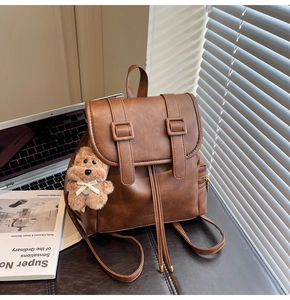 Detail of vintage brown mini PU leather backpack with decorative straps and plush dog charm