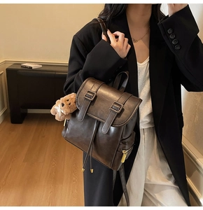 Detail of dark brown vintage leather backpack with drawstring and plush bear charm