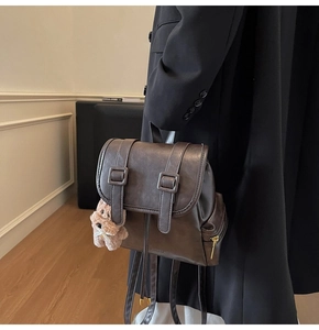Detail of dark brown retro backpack with decorative buckle straps and a cute bear charm