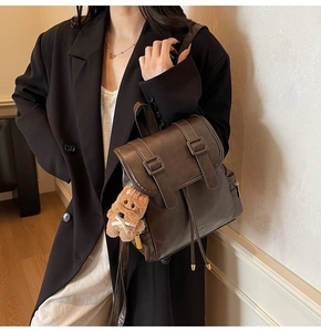 Detail of dark brown faux leather backpack with buckle closure and plush puppy charm