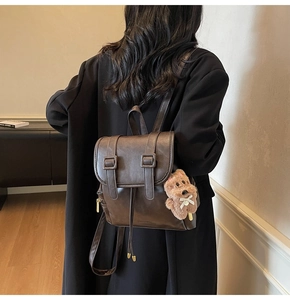 Detail of dark brown faux leather backpack with buckle straps and plush dog charm