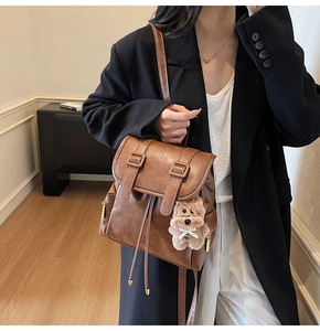 Detail of a brown leather backpack with drawstring closure and cute plush bear charm