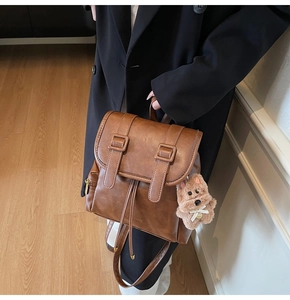Brown leather backpack featuring flap cover with dual straps and cute bear pendant