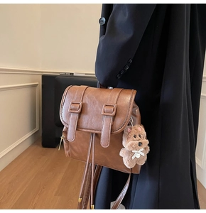 Detail of a brown faux leather backpack with buckle straps and a cute plush dog charm