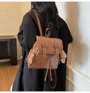 Detail of a brown faux leather backpack with drawstring closure and plush bear pendant