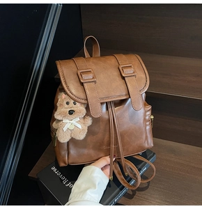 Close-up of brown leather backpack with drawstring closure and teddy bear charm