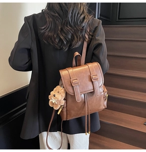Detail of a brown PU leather backpack with buckle straps and a cute teddy bear charm