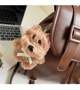 Brown plush animal charm with cream bow and golden tag on a brown leather backpack