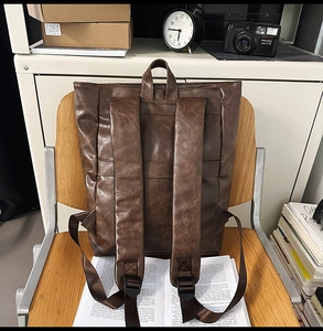 Détail de l'arrière du sac à dos en cuir marron avec bretelles réglables sur une chaise