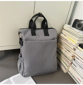 Détail du sac à dos en toile grise montrant les poches latérales et les poignées