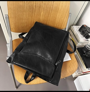 Détail du sac à dos rétro en similicuir noir avec poche frontale sur chaise en bois