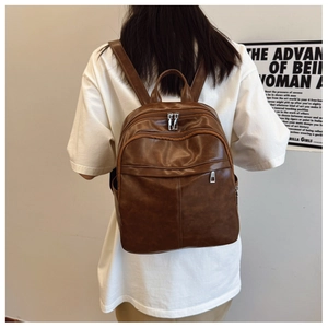 Rear view of model wearing a brown faux leather backpack with multi-zipper design