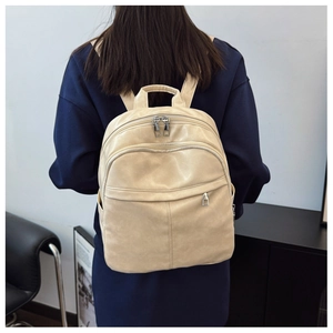 Detail view of cream faux leather backpack showing multiple compartments and smooth texture