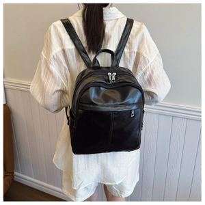 Rear view of model wearing a black PU leather backpack with silver zippers and side pockets