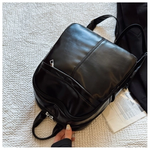 Detail of a sleek black faux leather backpack with silver zippers on a soft white texture