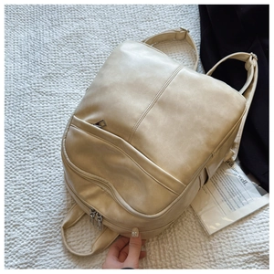 Detail shot of a minimalist cream PU leather backpack with sleek stitching on textured fabric