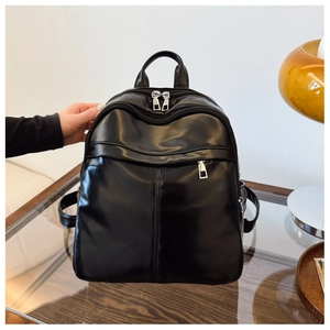 Detail of black faux leather backpack featuring dual metal zippers and a front pocket
