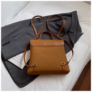 Detail view of the brown leather backpack back straps and metal hardware on soft bedding