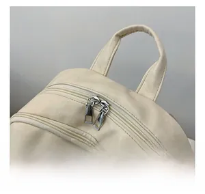 Close-up of smooth cream PU leather backpack featuring dual silver metal zippers and top handle