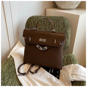 Detail of vintage dark brown faux leather backpack with silver lock on a green chair