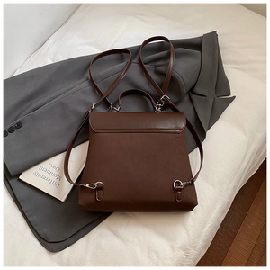 Detail view of brown matte backpack with silver hardware and detachable straps on white fabric