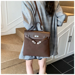 Detail of a dark brown leather handbag with metal turn-lock closure on grey suit