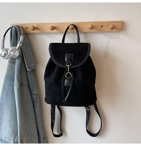 Detail of matte black backpack with metal buckle and top handle in a cozy home setting